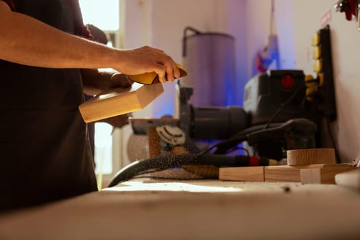 Artisan in studio using sandpaper for smoothing wooden surface, creating wood art designs, enjoying diy hobby. Man using sanding sheets to refurbish damages suffered by timber block, close up shot