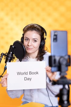 Woman filming promotional video for world book day using microphone and phone, studio background. Content creator promoting reading, gaining awareness for literature importance