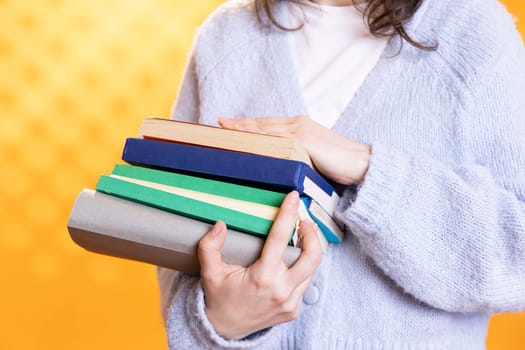 Woman carrying stack of books, gathering information for school exam, isolated over studio background, close up shot. Student holding pile of books, preparing school homework