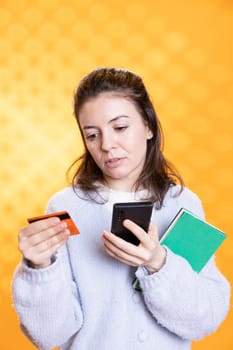 Woman appalled by books cost while adding credit card information on cellphone, studio background. Person balking at high price of academic textbook needed for university classes, using phone