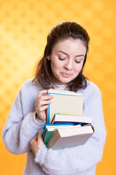Portrait of joyous woman browsing through stack of books, gathering information for school exam, studio background. Radiant student rummaging through textbooks pile, preparing for courses