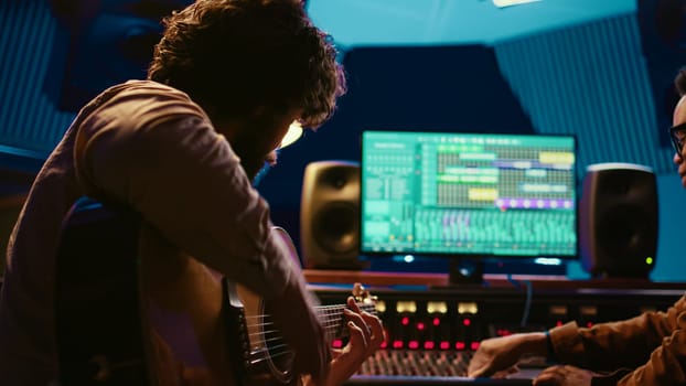 Young artist songwriter composing a new song on guitar in recording session at studio, creating tunes and editing them after in post production. Musician composer producing tracks. Camera B.