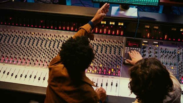 Music production team examining volume levels on audio software, using mixing and mastering techniques to create a hit song. Musician and sound designer work on editing recorded tracks. Camera B.