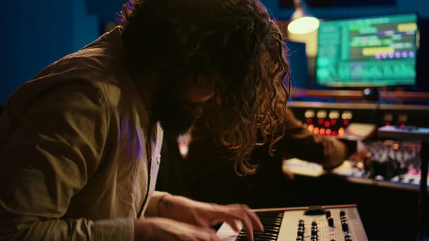 Singer performer creating a song on piano midi controller in studio, recording notes on electronic keyboard. Artist musician composing and producing tracks with technician. Camera B.