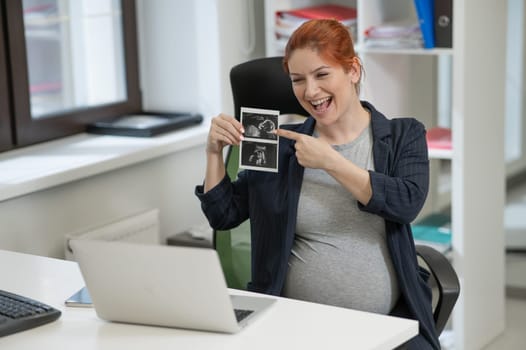 A pregnant woman shows a photo from an ultrasound scan of the fetus via video link in the office