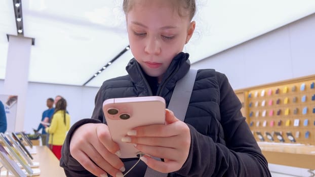 Denver, Colorado, USA-March 23, 2024-curious little girl examines the latest iPhone models on display at the Apple Store located in Park Meadows Mall, showcasing a youthful interest in technology.