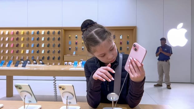 Denver, Colorado, USA-March 23, 2024-curious little girl examines the latest iPhone models on display at the Apple Store located in Park Meadows Mall, showcasing a youthful interest in technology.