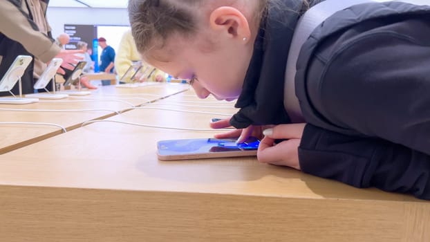 Denver, Colorado, USA-March 23, 2024-curious little girl examines the latest iPhone models on display at the Apple Store located in Park Meadows Mall, showcasing a youthful interest in technology.