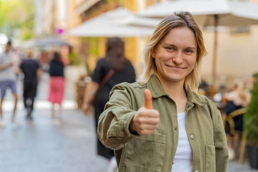 Like. Happy pretty young woman looking approvingly at camera showing thumbs up like sign positive something good positive feedback. Excited Girl celebrate success on city street. Town lifestyles.