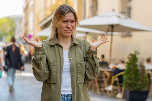 I don't know what to say. Confused young woman feeling embarrassed about ambiguous question, having doubts, no idea, being clueless uncertain. Portrait of girl standing on urban city street outdoors.