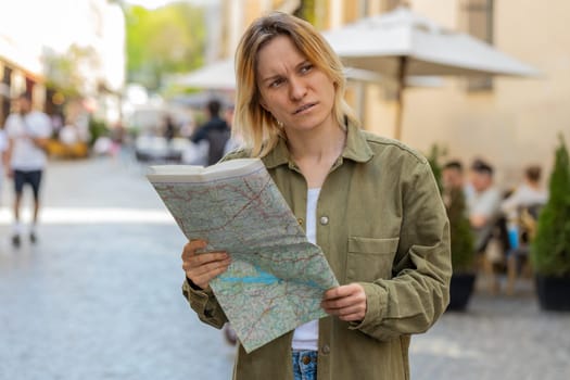 Caucasian young woman traveler lost while traveling in city, exploring sightseeing, navigating, looking way destination outdoors. Girl holding tourist paper map walking on street. Town lifestyles.