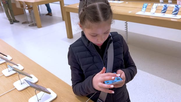 Denver, Colorado, USA-March 23, 2024-curious little girl examines the latest iPhone models on display at the Apple Store located in Park Meadows Mall, showcasing a youthful interest in technology.