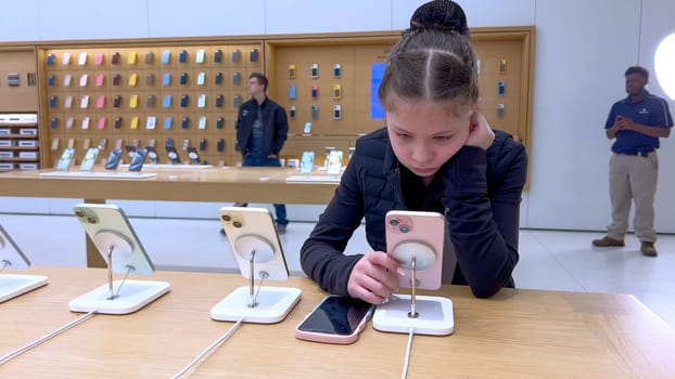 Denver, Colorado, USA-March 23, 2024-curious little girl examines the latest iPhone models on display at the Apple Store located in Park Meadows Mall, showcasing a youthful interest in technology.