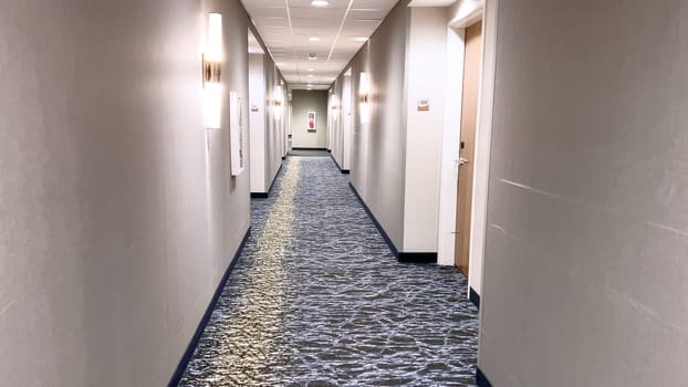 Ft Collins, Colorado, USA-March 23, 2024-A well-lit hallway stretches into the distance in a modern hotel, featuring elegant carpeting, clean lines, and a series of numbered doors on either side.