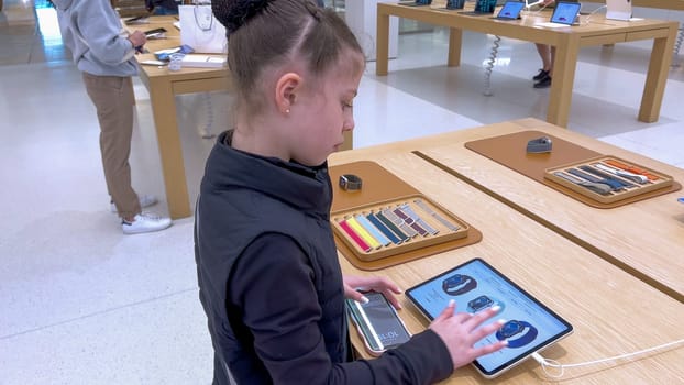 Denver, Colorado, USA-March 23, 2024-curious little girl examines the latest iPhone models on display at the Apple Store located in Park Meadows Mall, showcasing a youthful interest in technology.