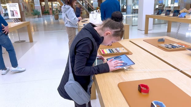 Denver, Colorado, USA-March 23, 2024-curious little girl examines the latest iPhone models on display at the Apple Store located in Park Meadows Mall, showcasing a youthful interest in technology.