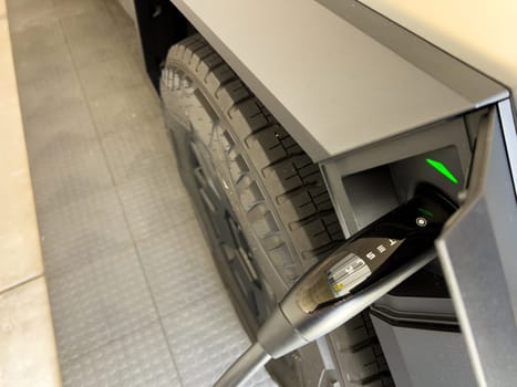 Denver, Colorado, USA-March 28, 2024-close-up view of a Tesla Cybertruck being charged, with the connector firmly plugged in, as indicated by the illuminated green lights, in a private suburban house garage.