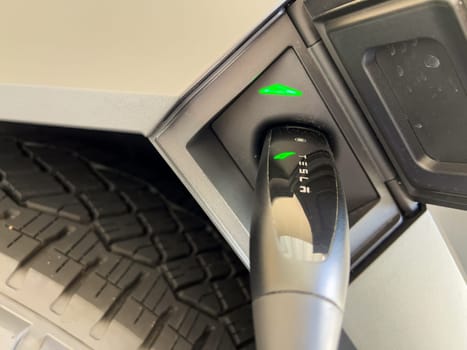 Denver, Colorado, USA-March 28, 2024-close-up view of a Tesla Cybertruck being charged, with the connector firmly plugged in, as indicated by the illuminated green lights, in a private suburban house garage.