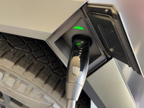 Denver, Colorado, USA-March 28, 2024-close-up view of a Tesla Cybertruck being charged, with the connector firmly plugged in, as indicated by the illuminated green lights, in a private suburban house garage.