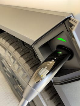 Denver, Colorado, USA-March 28, 2024-close-up view of a Tesla Cybertruck being charged, with the connector firmly plugged in, as indicated by the illuminated green lights, in a private suburban house garage.