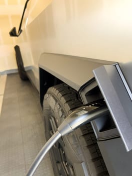 Denver, Colorado, USA-March 28, 2024-close-up view of a Tesla Cybertruck being charged, with the connector firmly plugged in, as indicated by the illuminated green lights, in a private suburban house garage.