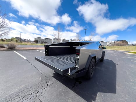 Denver, Colorado, USA-March 28, 2024-The distinctive rear end of a Tesla Cybertruck, captured in an empty parking lot, stands out against a backdrop of suburban homes under a blue sky with fluffy clouds.