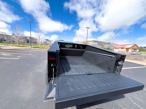 Denver, Colorado, USA-March 28, 2024-The distinctive rear end of a Tesla Cybertruck, captured in an empty parking lot, stands out against a backdrop of suburban homes under a blue sky with fluffy clouds.