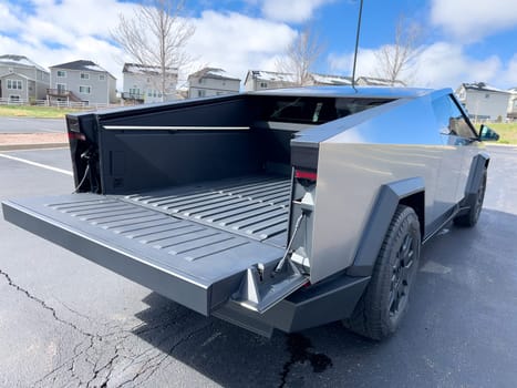 Denver, Colorado, USA-March 28, 2024-The distinctive rear end of a Tesla Cybertruck, captured in an empty parking lot, stands out against a backdrop of suburban homes under a blue sky with fluffy clouds.