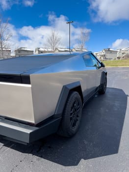 Denver, Colorado, USA-March 28, 2024-The distinctive rear end of a Tesla Cybertruck, captured in an empty parking lot, stands out against a backdrop of suburban homes under a blue sky with fluffy clouds.