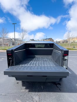 Denver, Colorado, USA-March 28, 2024-The distinctive rear end of a Tesla Cybertruck, captured in an empty parking lot, stands out against a backdrop of suburban homes under a blue sky with fluffy clouds.