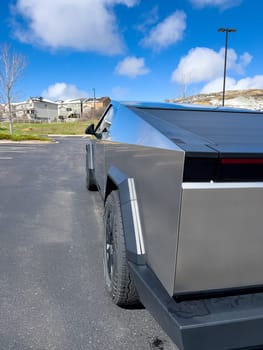 Denver, Colorado, USA-March 28, 2024-The distinctive rear end of a Tesla Cybertruck, captured in an empty parking lot, stands out against a backdrop of suburban homes under a blue sky with fluffy clouds.