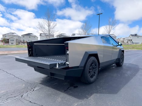 Denver, Colorado, USA-March 28, 2024-The distinctive rear end of a Tesla Cybertruck, captured in an empty parking lot, stands out against a backdrop of suburban homes under a blue sky with fluffy clouds.