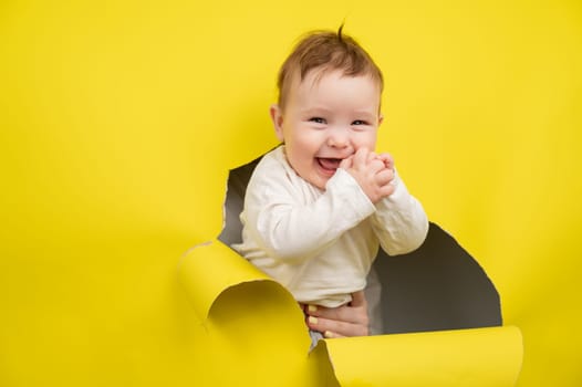Cheerful baby rips and sticks out through yellow cardboard background