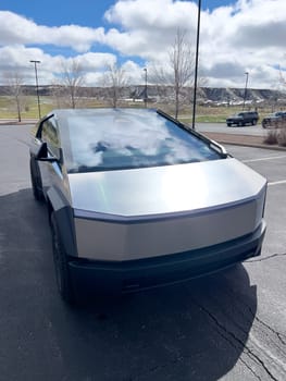 Denver, Colorado, USA-March 28, 2024-The front profile of a Tesla Cybertruck is displayed, showcasing its futuristic lines and robust design, parked in an open-air parking lot with a dynamic sky overhead.