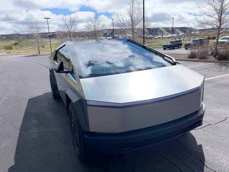 Denver, Colorado, USA-March 28, 2024-The front profile of a Tesla Cybertruck is displayed, showcasing its futuristic lines and robust design, parked in an open-air parking lot with a dynamic sky overhead.