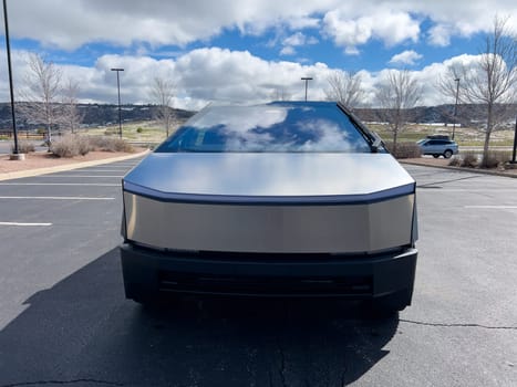 Denver, Colorado, USA-March 28, 2024-The front profile of a Tesla Cybertruck is displayed, showcasing its futuristic lines and robust design, parked in an open-air parking lot with a dynamic sky overhead.