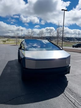 Denver, Colorado, USA-March 28, 2024-The front profile of a Tesla Cybertruck is displayed, showcasing its futuristic lines and robust design, parked in an open-air parking lot with a dynamic sky overhead.