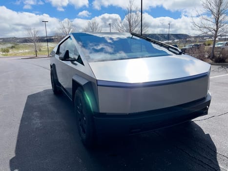 Denver, Colorado, USA-March 28, 2024-The front profile of a Tesla Cybertruck is displayed, showcasing its futuristic lines and robust design, parked in an open-air parking lot with a dynamic sky overhead.