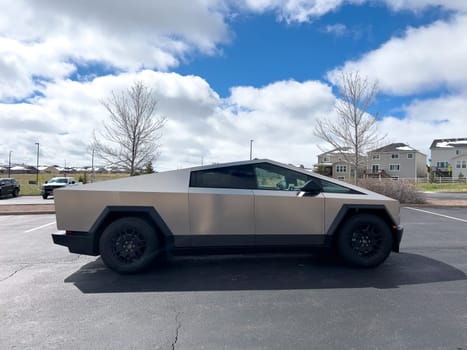 Denver, Colorado, USA-March 28, 2024-Captured from the side, a Tesla Cybertruck stands prominently in a vast parking lot, reflecting the innovation of electric vehicles against a serene, natural backdrop.