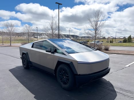 Denver, Colorado, USA-March 28, 2024-Captured from the side, a Tesla Cybertruck stands prominently in a vast parking lot, reflecting the innovation of electric vehicles against a serene, natural backdrop.