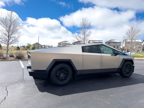 Denver, Colorado, USA-March 28, 2024-Captured from the side, a Tesla Cybertruck stands prominently in a vast parking lot, reflecting the innovation of electric vehicles against a serene, natural backdrop.