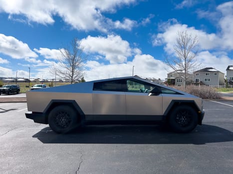 Denver, Colorado, USA-March 28, 2024-Captured from the side, a Tesla Cybertruck stands prominently in a vast parking lot, reflecting the innovation of electric vehicles against a serene, natural backdrop.