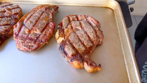 Three succulent ribeye steaks display perfect grill marks after being cooked, presented on a neutral surface, embodying the art of grilling.