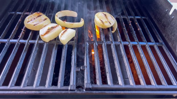 Ribeye steaks are sizzling alongside golden grilled onions on a barbecue grill, with wisps of smoke hinting at the flavorful feast being prepared.