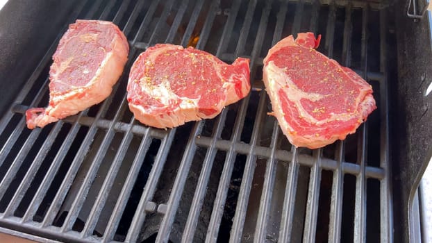 Ribeye steaks are sizzling alongside golden grilled onions on a barbecue grill, with wisps of smoke hinting at the flavorful feast being prepared.