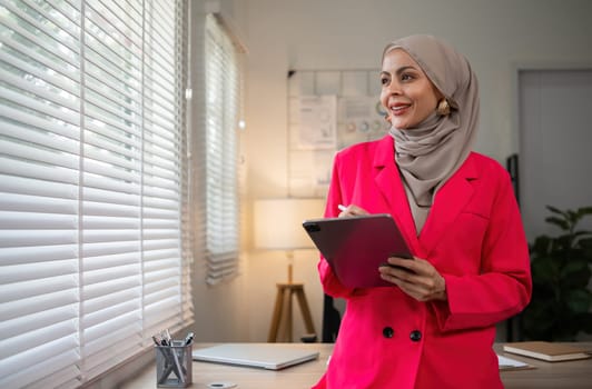 Confident Muslim businesswoman standing in front of desk in office.