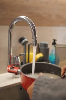 A person is using the kitchen sink to wash a pot with water from the tap. The plumbing fixture is located on the countertop, and the liquid is flowing into the sink