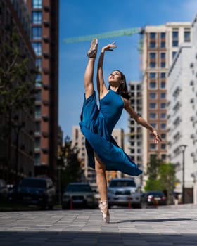 Beautiful Asian ballerina in blue dress posing in splits outdoors. Urban landscape. Vertical photo
