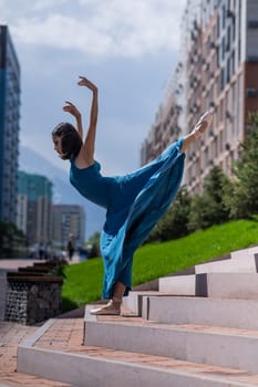 Beautiful Asian ballerina in blue dress posing on stairs outdoors. Urban landscape. Vertical photo