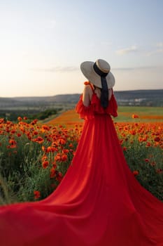 Woman poppy field red dress hat. Happy woman in a long red dress in a beautiful large poppy field. Blond stands with her back posing on a large field of red poppies